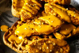A delicious plant-based dish with crispy vegan chick'n tenders on top of whole grain waffles, drizzled with a zesty maple sriracha mustard sauce.