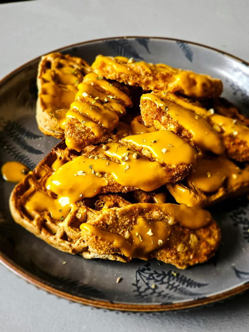 A delicious plant-based dish with crispy vegan chick'n tenders on top of whole grain waffles, drizzled with a zesty maple sriracha mustard sauce.